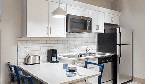 Modern kitchen with white cabinets, stainless steel appliances, a countertop with a toaster, coffee maker, blue chairs, a plate, cup, and a magazine.