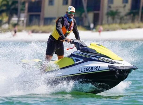 A person wearing a life jacket and sunglasses rides a yellow and white jet ski with 