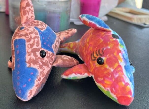 Two colorful, patterned stuffed toy dolphins with black button eyes sit side by side on a black surface.