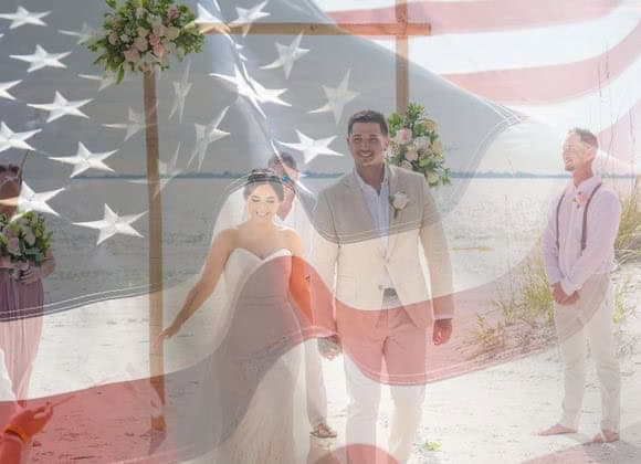 A bride and groom walk on a beach during their wedding ceremony, with an overlay of the American flag across the image.