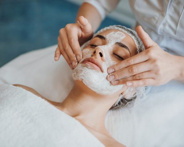 An aesthetician applying a facial mask to a client.