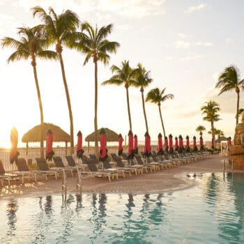 A row of lounge chairs and pink umbrellas beside a swimming pool with a large rock formation shaped like an octopus.
