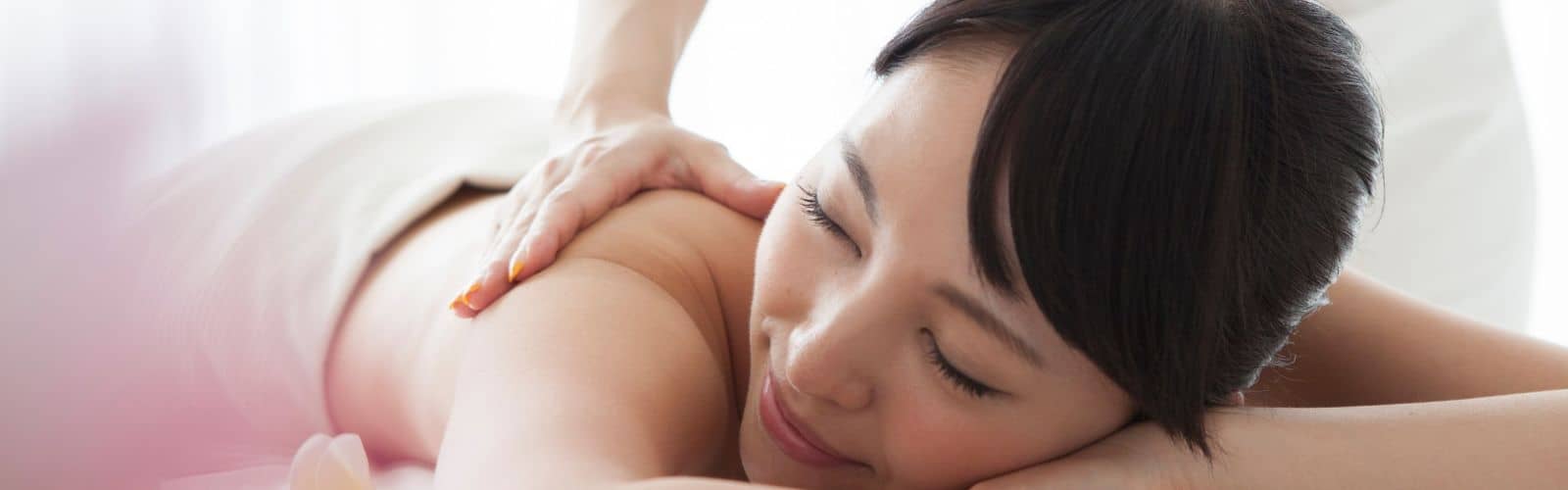 A woman with eyes closed receiving a shoulder massage.