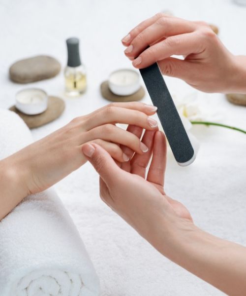 A manicurist using a nail file on a client’s fingernail.